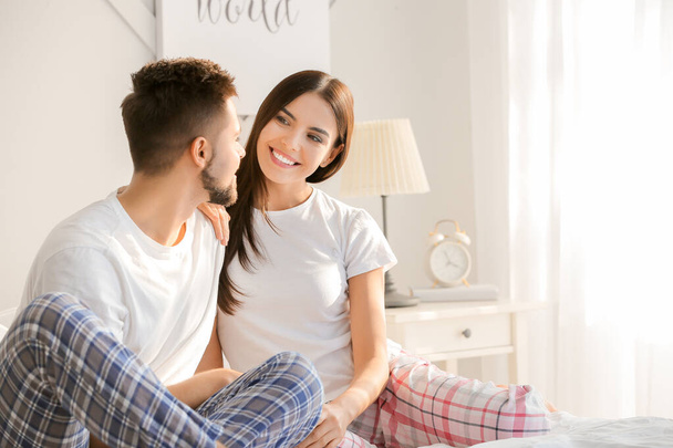 Beautiful young couple sitting on bed at home - Foto, imagen