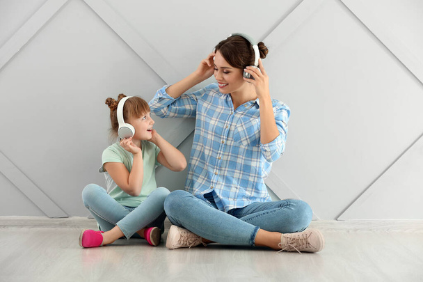 Portrait of happy mother and daughter listening to music on grey background - Photo, Image