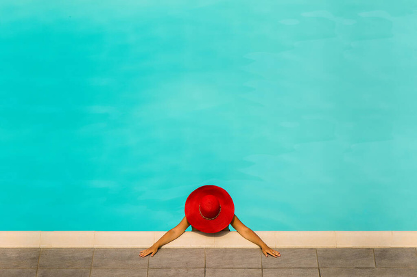 Hermosa chica en un traje de baño y un sombrero rojo en una piscina de agua azul
 - Foto, imagen