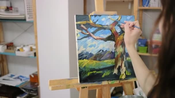 Kobieta rysuje szerokimi pociągnięciami farb na płótnie, przedstawiającymi krajobraz - Materiał filmowy, wideo