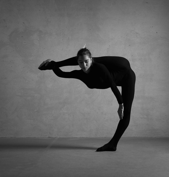 Siyah kostümlü esnek bir jimnastikçi. Siyah beyaz fotoğraf. - Fotoğraf, Görsel
