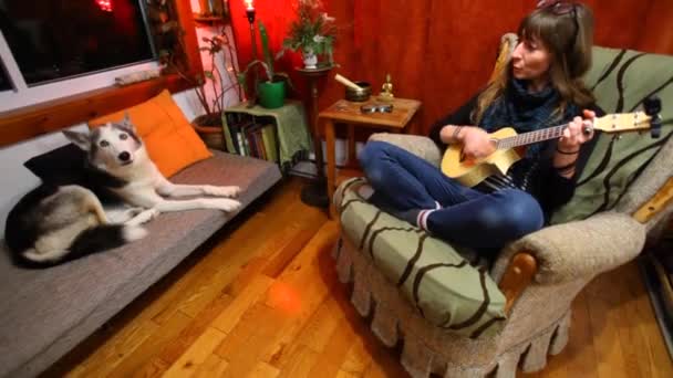 Dziewczyna gra ukulele w salonie.  - Materiał filmowy, wideo
