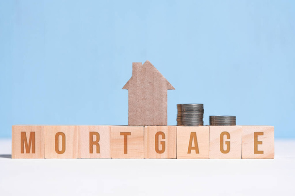 Cardboard cutout house and coins on cubes with inscription mortgage on blue background. - Foto, Imagen