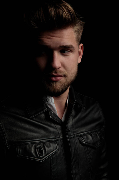 casual man wearing black leather jacket looking away curious - 写真・画像