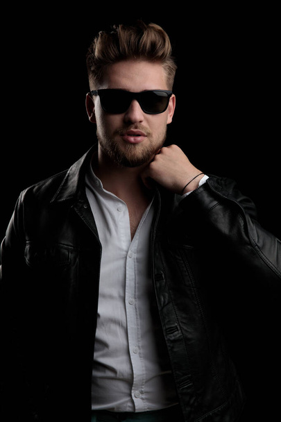 casual man wearing sunglasses standing and fixing his collar - Фото, изображение