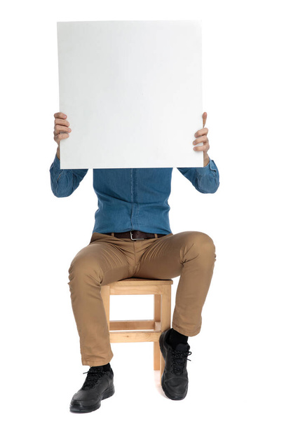šťastný mladý muž zakrývající tvář s prázdnou deskou - Fotografie, Obrázek