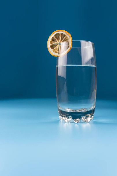 Glas water met een schijfje gedroogde citroen op een blauwe achtergrond - Foto, afbeelding