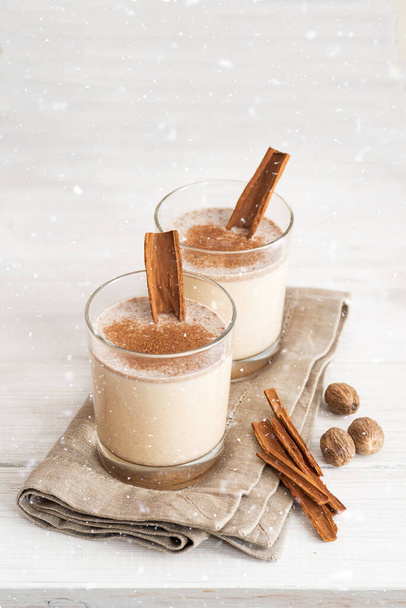 Eggnog in glass cups with a delicate foam, spices and a cinnamon stick - Photo, Image