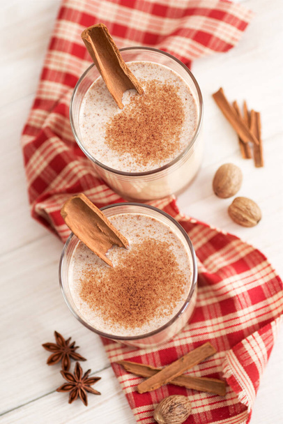 Eggnog in glass cups with a delicate foam, spices and a cinnamon stick - Foto, afbeelding
