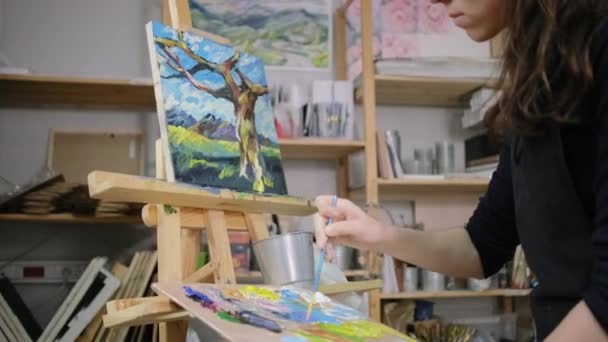 Paintress is depicting tree trunk on picture with landscape in studio - Footage, Video
