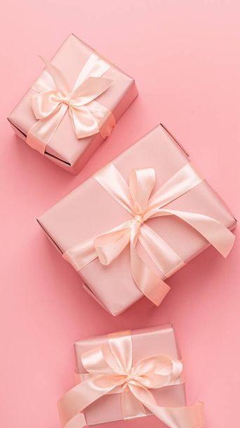 Holiday gift boxes with satin ribbon bow on a pastel pink background. Festive minimalism concept. Flat style layout. - Photo, Image
