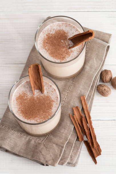 Eggnog in glass cups with a delicate foam, spices and a cinnamon stick - Fotoğraf, Görsel