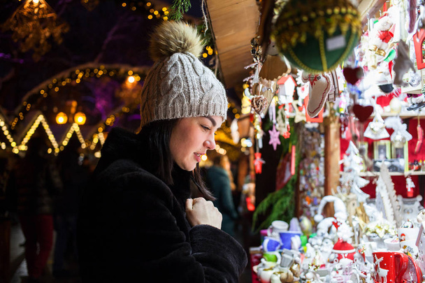 Счастливая молодая женщина выбирает рождественские украшения на рынке - Фото, изображение