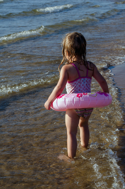 Kleines Mädchen mit rosafarbenem Schwimmer blickt vorsichtig ins Wasser - Foto, Bild