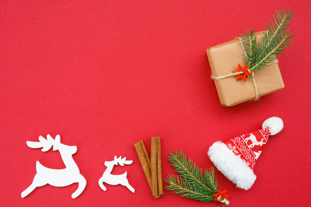 Joulun koostumus: mäntyoksat, lahjapakkaus, kanelitangot, puiset peurat ja jouluhattu punaisella taustalla. Tekstiavaruus. Huippunäkymä. Litteä
 - Valokuva, kuva