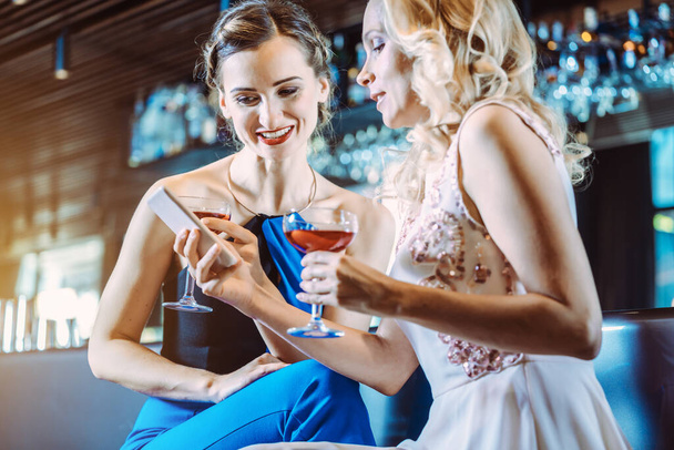 Két nő egy bárban nézi a mobilját. - Fotó, kép