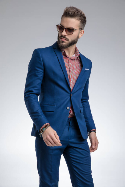 cool dramatic guy in blue suit wearing sunglasses and walking - Photo, Image