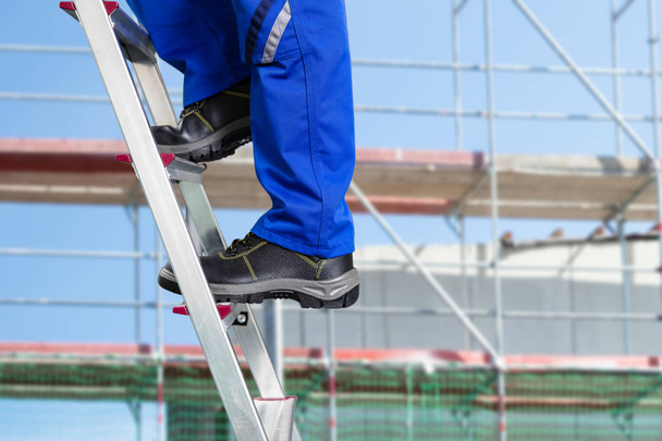 Close-up Of A Handy Repair Man Standing On Steel Ladder Against Construction Sites - Photo, Image