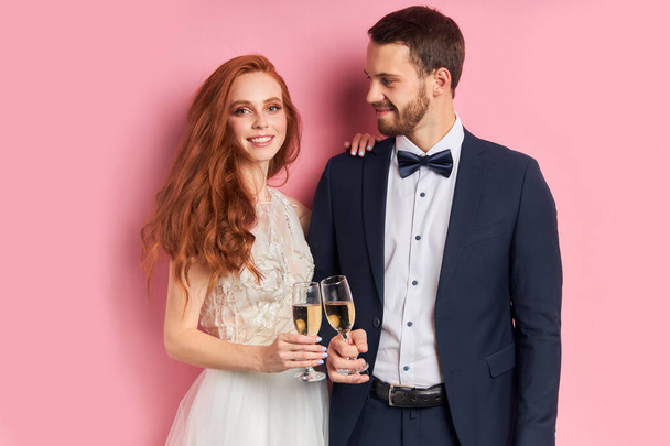 Smiling wedding couple with champagne isolated over pink background - Фото, изображение