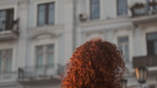 Excited beautiful young redhead curly woman smiling and spinning around while walking at the street - Filmati, video
