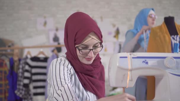 Joven diseñadora de moda musulmana en pañuelo nacional cose en una máquina de coser
 - Metraje, vídeo