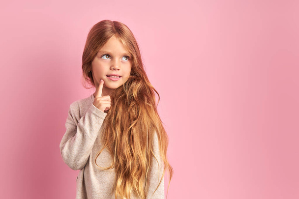 Thoughtful little girl dreaming isolated over pink background - Fotografie, Obrázek