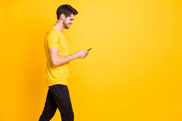 Photo of cheerful trendy positive handsome attractive man addicted to browsing through his profile in social media wearing t-shirt black trousers isolated vivid color background - Zdjęcie, obraz