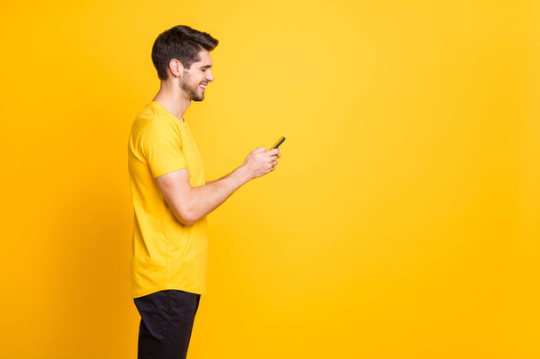 Profil fotó a fiatal jóképű srác gazdaság telefon csevegés barátok megvitatása jövőbeli diákok fél viselet alkalmi póló elszigetelt sárga háttér - Fotó, kép