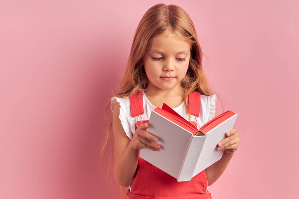Mindful girl attentively read book isolated over pink background - Photo, Image