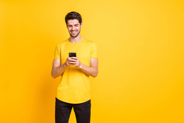 Photo of handsome attractive man browsing through his phone in search of new information reading feednews isolated over yellow vivid color background - Φωτογραφία, εικόνα