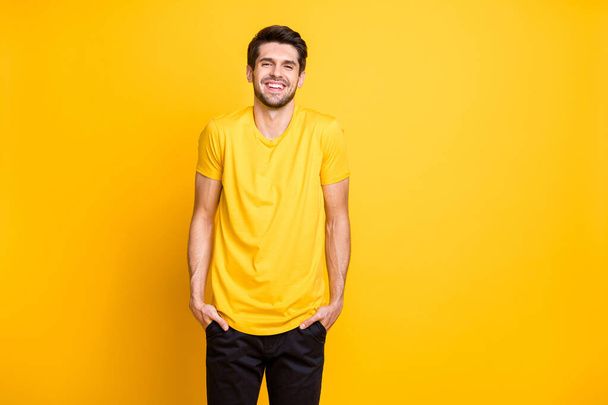 Photo of amazing handsome guy holding hands in pockets cool summer mood going outside meet friends wear casual t-shirt black pants isolated yellow color background - Foto, Bild
