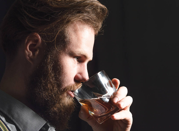 Portrait of a handsome young man with a beard drinking alcohol from a glass. - Фото, зображення