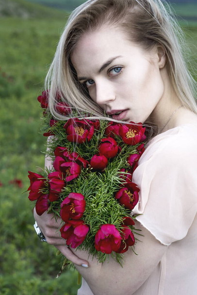 Beautiful blonde girl with flowers in her hands in the field. - Fotó, kép