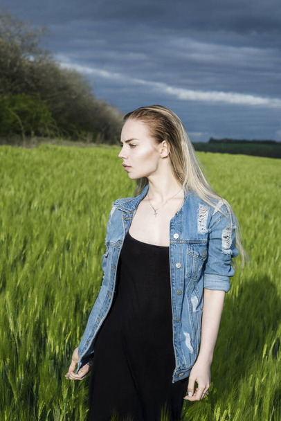 schöne blonde Mädchen steht auf einem Feld vor einem Hintergrund aus Wolken. - Foto, Bild
