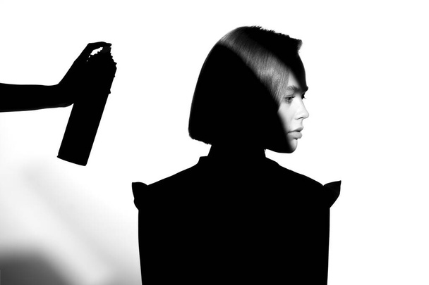 Black and white silhouette portrait with shadow and spot of light. The girl uses hairspray. Hair cosmetic concept. - 写真・画像