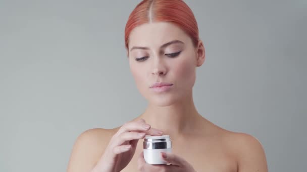 Studio portrait of young, beautiful and natural redhead woman applying skin care cream. Face lifting, cosmetics and make-up concept. - Materiaali, video