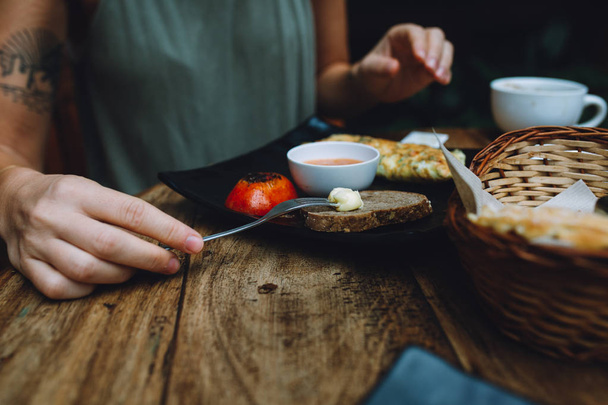 Een close-up van een vrouw die haar ontbijt opeet in een café. Brood, vegetarische omlette en tomaat op basis van zetmeel. - Foto, afbeelding