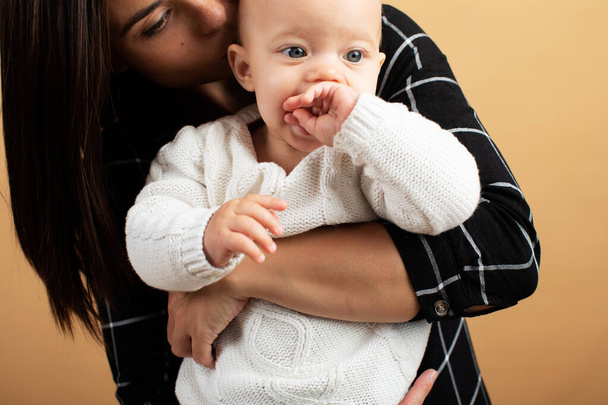 junge und energische Mutter umarmt und küsst ihr Baby auf orangefarbenem Hintergrund - Foto, Bild