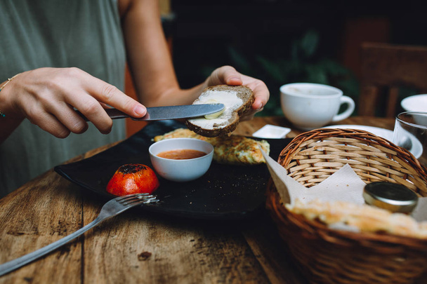 Primer plano de una mujer desayunando en un café. Pan, omlette vegetariano y tomate respaldado
. - Foto, imagen