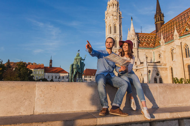 Young couple searching right direction on map from the point from Fisherman Bastion in Budapest with Matthias Church on background - Zdjęcie, obraz