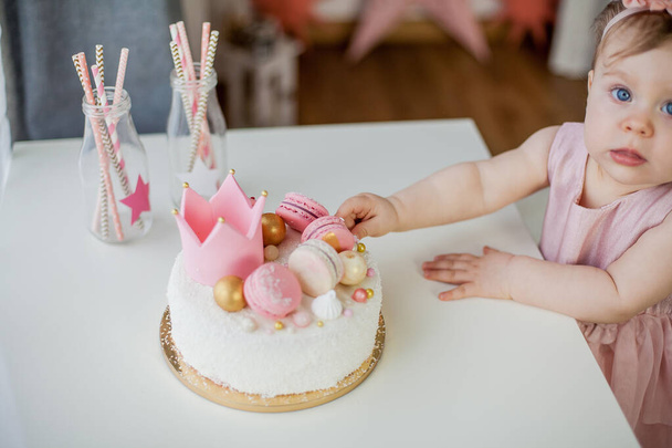 Primer cumpleaños. Pequeña chica hermosa en un vestido rosa prueba su pastel de cumpleaños. Fiesta de cumpleaños
. - Foto, imagen