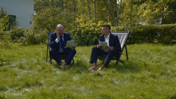 Männer in Anzügen sitzen mit Papieren im Hof und unterhalten sich. - Foto, Bild