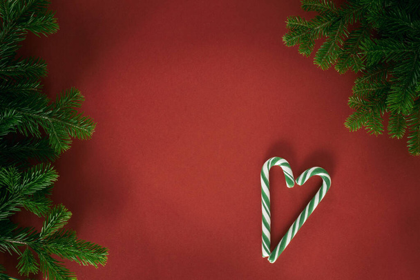 Christmas composition. Branches of spruce, lollipop cane in the shape of a heart on a red background. Christmas, winter, new year concept. Flat lay, top view, copy space. - Foto, immagini