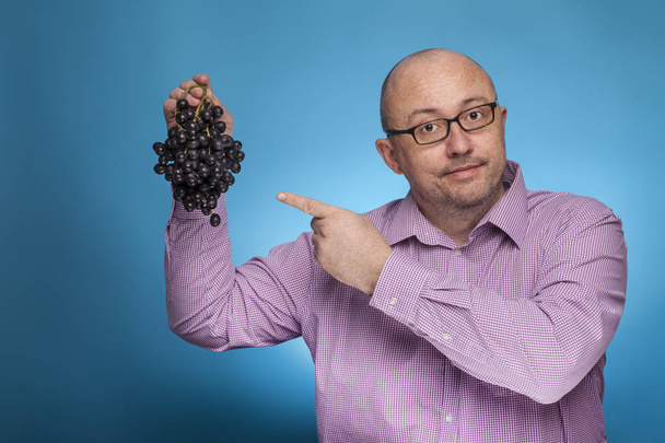 Een zakenman in een gespikkeld shirt houdt druiven in de hand - Foto, afbeelding
