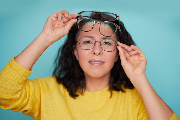 Happy funny girl in casual or hipster style, pigtail hairstyle, standing, holding two blue and pink glasses and looking away with toothy smile, Indoor studio shot, isolated on blue or green background - 写真・画像