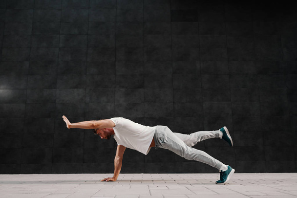 Handsome caucasian bearded man in tracksuit doing strength exercises for arms and legs on the ground. - 写真・画像
