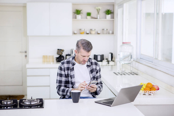 Caucasian man using a phone while works in kitchen - Photo, image
