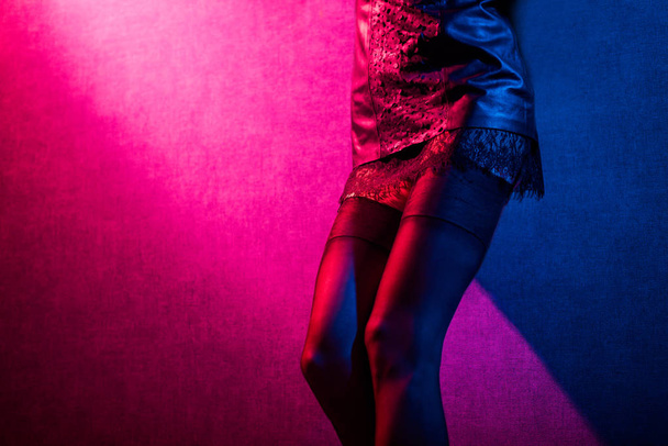 young sexy woman in stockings standing at wall in colorful red and blue light - Foto, imagen