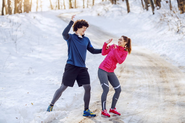 Speels Kaukasisch sportief echtpaar in sportkleding dat plezier heeft in de sneeuw. Wintertijd. Outdoor fitness concept. - Foto, afbeelding