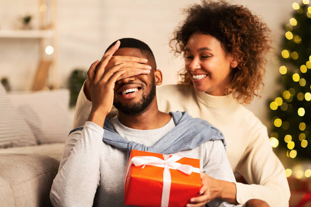 Weihnachtsgeschenk. Afrikanisch-amerikanische Frau überrascht Ehemann zu Hause - Foto, Bild